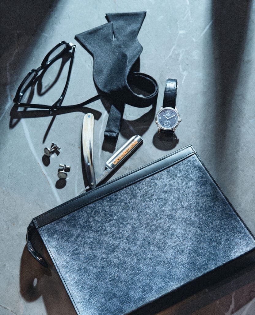 Estuche de viaje en tela de lona Damier Graphite, de LOUIS VUITTON. Navaja de barbería con mango de cuero, de LARUSMIANI. Gemelos de acero premium con logo, de MONTBLANC. Gafas de vista, de ZEGNA EYEWEAR. Pajarita de seda, de FUMAGALLI 1891. Reloj Perpetual 1908 en oro blanca con caja de 39 mm, de ROLEX. 