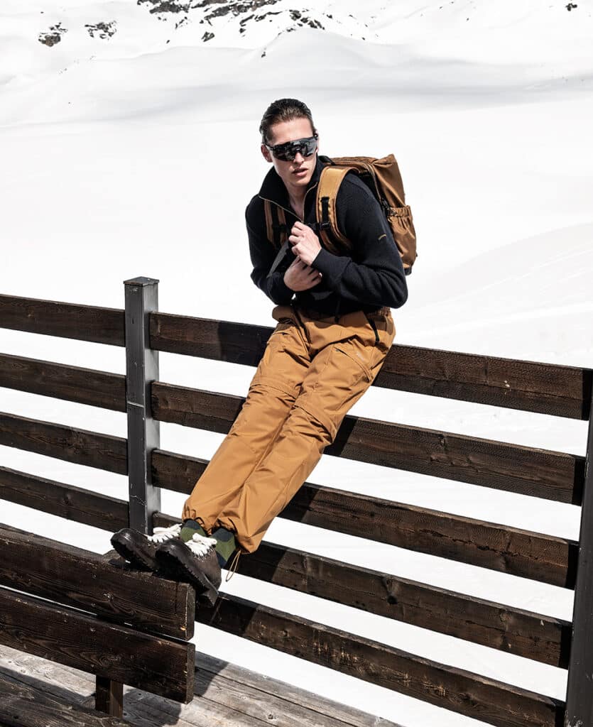 Jersey de lana con cremallera; pantalón con cordón; y mochila técnica, todo de PAUL & SHARK. Botas de cuero con cordones, de DOUCAL. Gafas de espejo, de BRIKO.